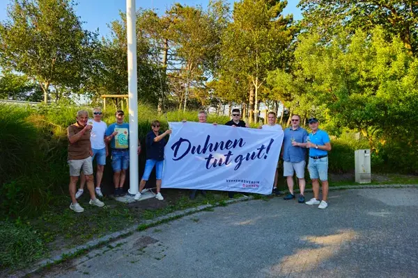 Gruppe von Personen hält Banner „Duhnen tut gut!“ im Freien.