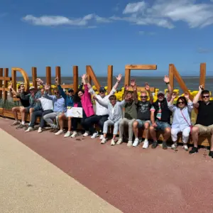 Gruppe feiert mit Zertifikat vor Duhnen-Schriftzug am Strand