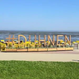 Holzschriftzug #DUHNEN am Strand mit gelben Strandkörben vor Wattenmeer.