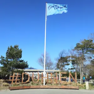 Holzschriftzug #DUHNEN mit hellblauer Flagge vor blauem Himmel