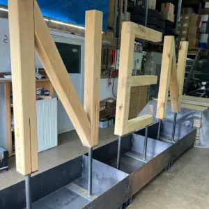 Große Holzbuchstaben 'NEN' in Metallkästen in einer Werkstatt.