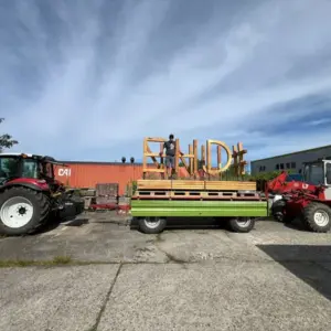 Traktor mit Anhänger, der große Holzbuchstaben „BOND#“ transportiert.
