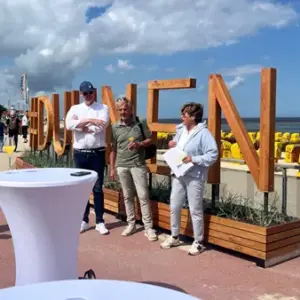 Menschengruppe vor Duhnen-Schriftzug an der Strandpromenade bei Sonnenschein.
