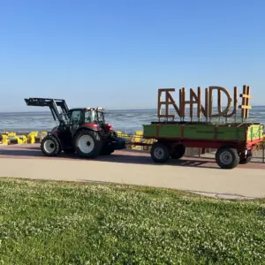 Traktor transportiert große Holzbuchstaben auf Anhänger an der Strandpromenade.
