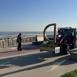 Traktor transportiert ein großes hölzernes 'D' auf einer Strandpromenade.