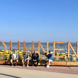 Vier Männer vor dem hölzernen Schriftzug #DUHNEN am Strand.