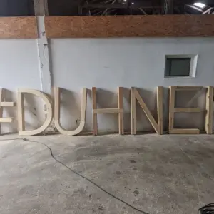 Große Holzbuchstaben bilden den Schriftzug #DUHNEN in einer Halle.