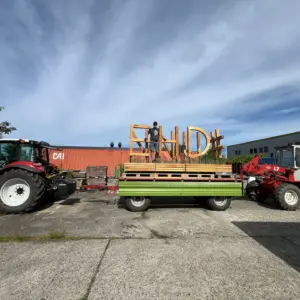 Hölzerner Schriftzug auf Anhänger zwischen Traktor und Radlader.