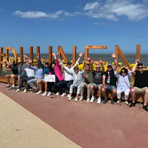 Gruppe winkt vor dem Schriftzug #DUHNEN am Strand.