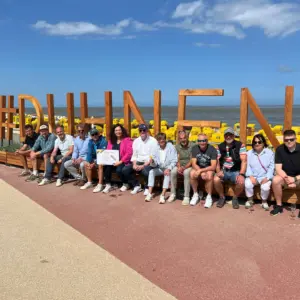 Gruppe sitzt vor großem hölzernen #DUENEN-Schriftzug am Strand.