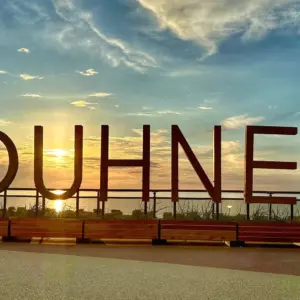 Großer #DUHNEN-Schriftzug aus Holz bei Sonnenuntergang am Meer.