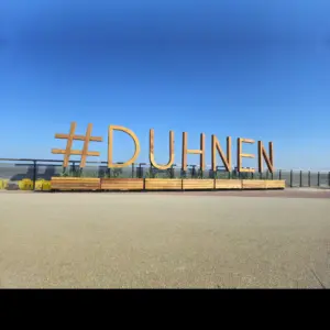 Hölzerner Schriftzug #DUHNEN auf der Strandpromenade vor blauem Himmel